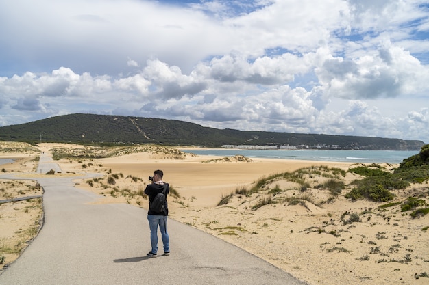 Mężczyzna fotograf spacerujący po plaży pod zachmurzonym niebem w ciągu dnia w Andaluzji w Hiszpanii