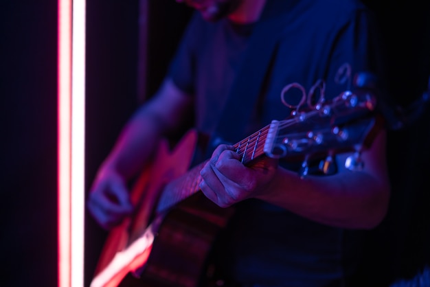Mężczyzna gra na gitarze akustycznej w ciemnym pokoju. Występ na żywo, koncert akustyczny.