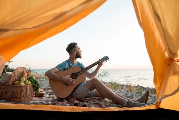 Mężczyzna gra na gitarze przed namiotem