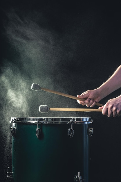 Bezpłatne zdjęcie mężczyzna gra na instrumencie perkusyjnym z pałeczkami na ciemnym tle