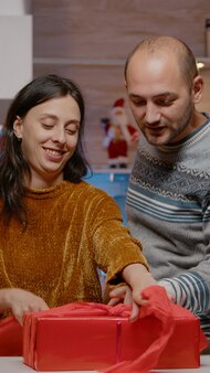 Mężczyzna i kobieta pakujący czerwony papier na prezent na celebrację wigilii. świąteczna para przygotowująca pudełko ozdobne wstążką na świąteczną uroczystość z przyjaciółmi i rodziną.
