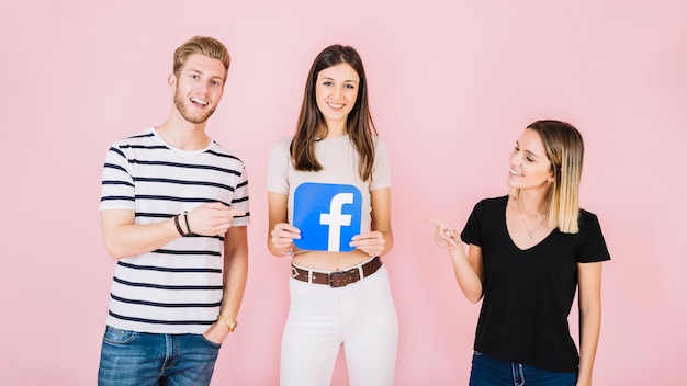 Mężczyzna i kobieta, wskazując na ich przyjaciel trzyma ikonę facebook na różowym tle