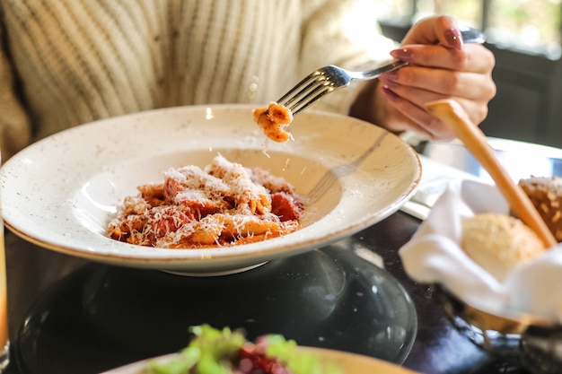 Mężczyzna je makaron penne z sosem pomidorowym, parmezanem, warzywami, mięsem, widok z boku