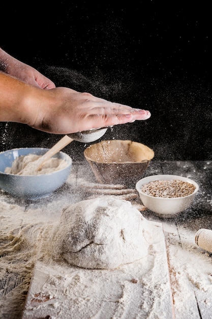 Mężczyzna kropi mąkę nad świeżym ciastem na kuchennym stole