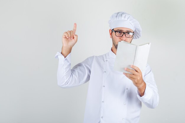 Mężczyzna kucharz czyta książkę i robi palec w białym mundurze