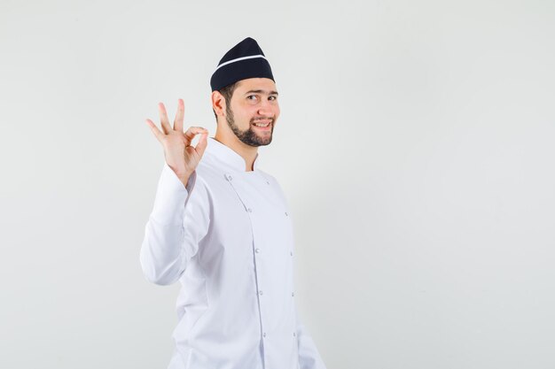 Mężczyzna kucharz pokazuje ok gest w białym mundurze i wygląda na zadowolonego. przedni widok.