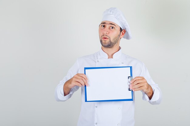 Mężczyzna kucharz trzyma schowek w białym mundurze i wygląda na zaskoczonego