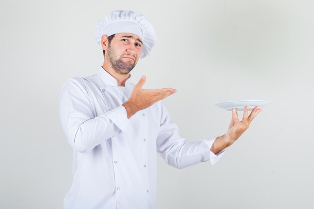 Mężczyzna kucharz trzyma talerz w białym mundurze i wygląda na niezadowolonego.