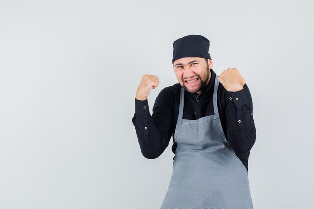 Mężczyzna kucharz w koszuli, fartuch pokazujący gest zwycięzcy i szczęśliwy, widok z przodu.