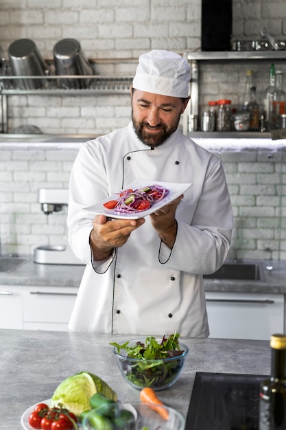 Mężczyzna kucharz w kuchni trzyma talerz sałatki