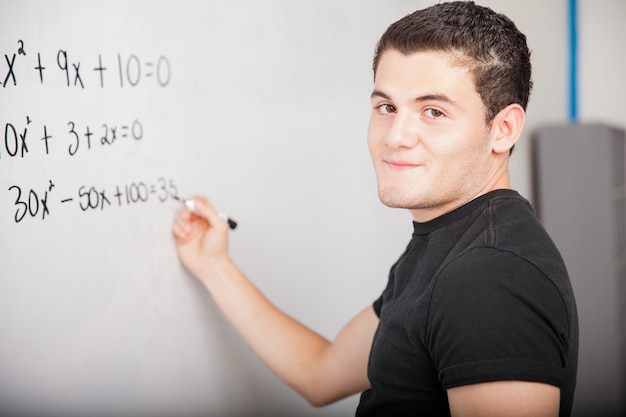 Bezpłatne zdjęcie mężczyzna latynoski uczeń liceum rozwiązujący pewne problemy matematyczne na białej tablicy w szkole