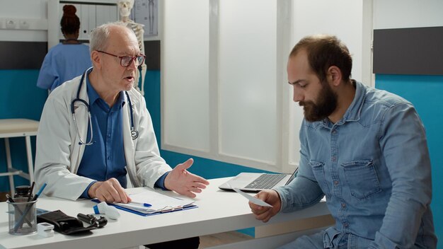 Mężczyzna lekarz daje papier na receptę choremu na wizytę kontrolną w gabinecie. Raport z badania z informacjami dotyczącymi opieki zdrowotnej i diagnozą choroby, leczenie w celu wyleczenia choroby.