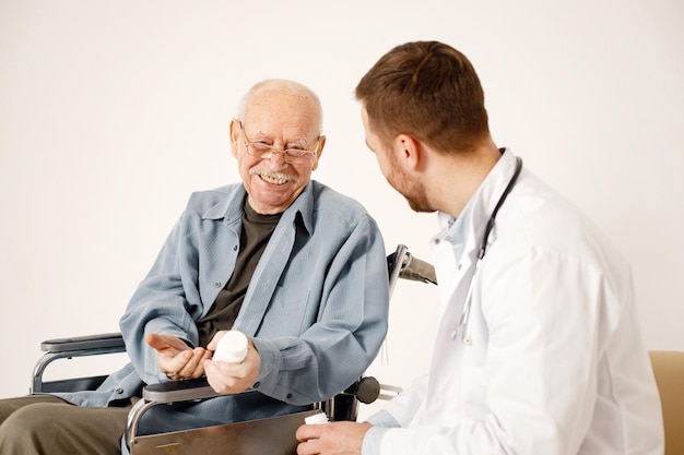 Mężczyzna lekarz i staruszek na wózku inwalidzkim na białym tle