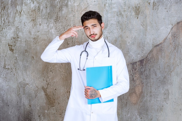 Mężczyzna lekarz trzyma niebieską folder ze stetoskopem, myśląc i planując.