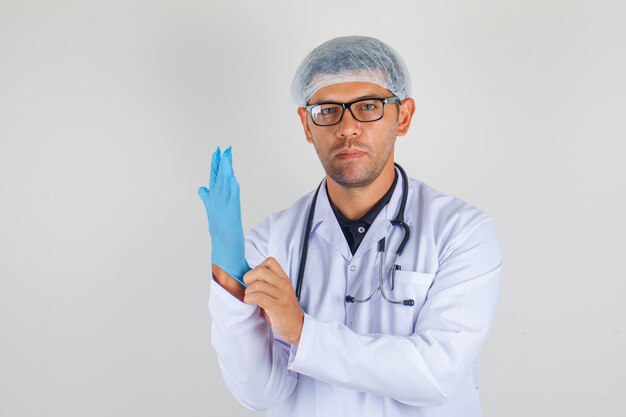 Mężczyzna lekarz w białej szacie medycznej, zakładając rękawicę i patrząc zamyślony