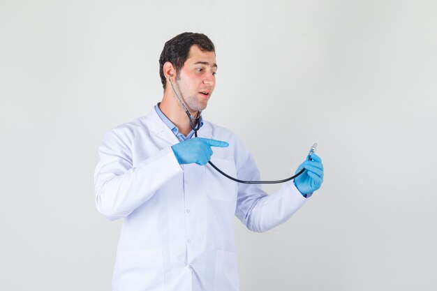 Mężczyzna lekarz w białym fartuchu, rękawiczki wskazując palcem na stetoskop