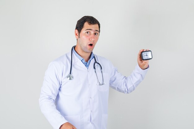 Mężczyzna lekarz w białym fartuchu trzymając zegar i patrząc zaskoczony