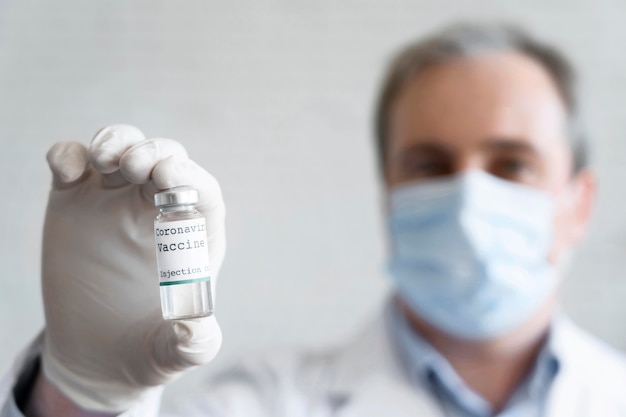 Bezpłatne zdjęcie mężczyzna lekarz z maseczką medyczną trzyma szczepionkę