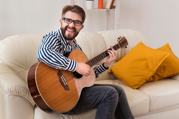 Mężczyzna na kanapie w domu, gra na gitarze