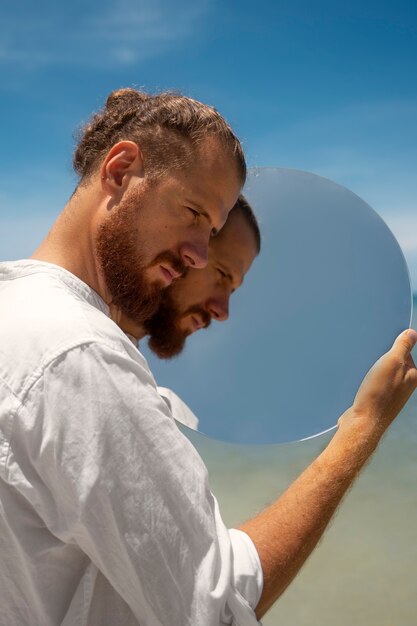 Mężczyzna na plaży pozuje z okrągłym odblaskowym lustrem