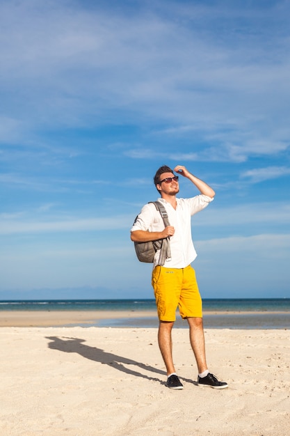 Mężczyzna na plaży uśmiechnięty i ubrany w jasny strój hipster