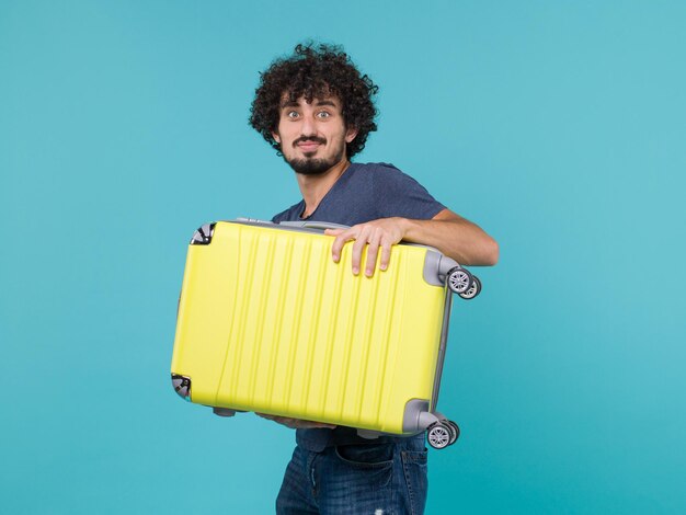 mężczyzna na wakacjach trzymający dużą żółtą walizkę na niebiesko