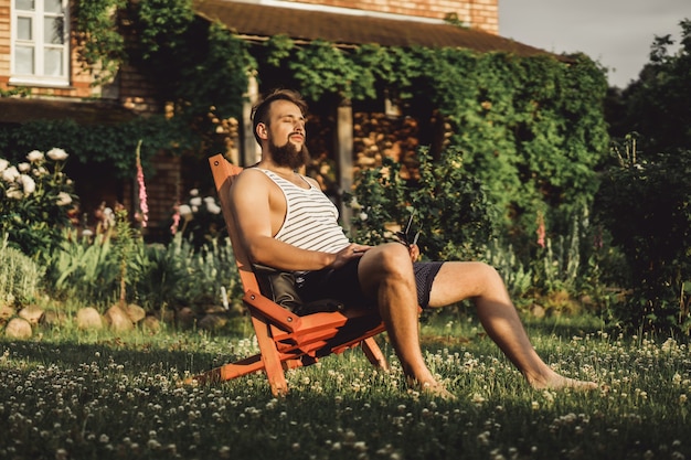 mężczyzna odpoczywa w wiejskim domu. Brodaty mężczyzna cieszy się zachód słońca na zielonym trawniku.