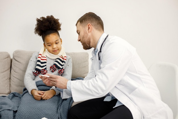 Mężczyzna pediatra badający chorą małą czarną dziewczynkę