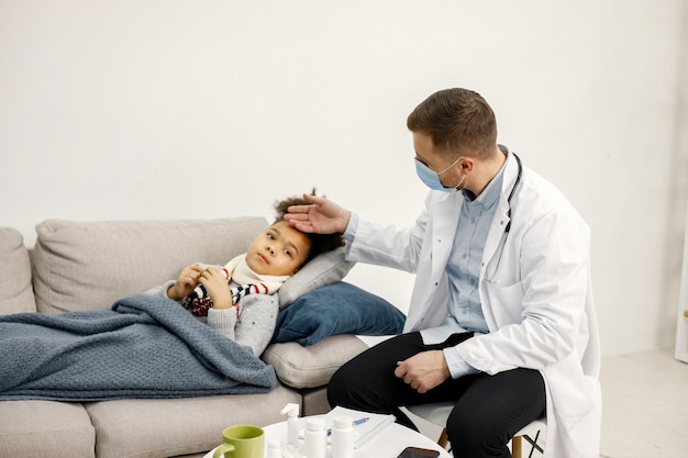 Bezpłatne zdjęcie mężczyzna pediatra trzymający rękę na czole chorej małej czarnej dziewczynki