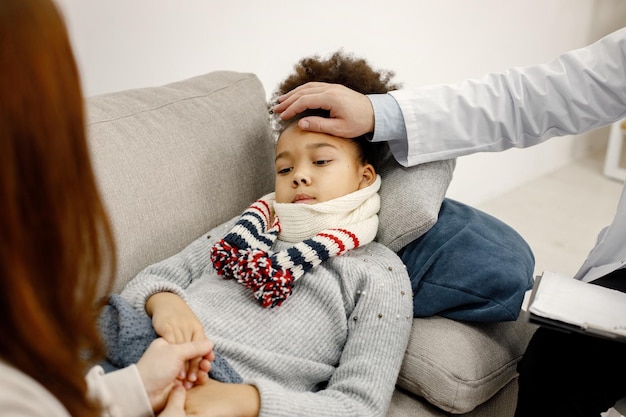 Mężczyzna pediatra trzymający rękę na czole chorej małej czarnej dziewczynki