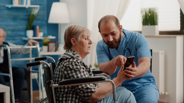 Mężczyzna pielęgniarka uczy emerytowaną kobietę z niepełnosprawnością obsługi smartfona