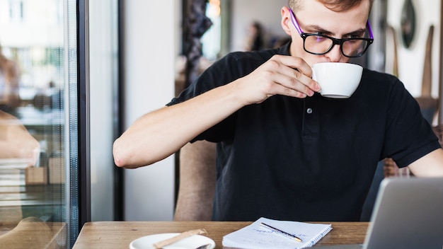 Bezpłatne zdjęcie mężczyzna pije kawę przy stołem z laptopem
