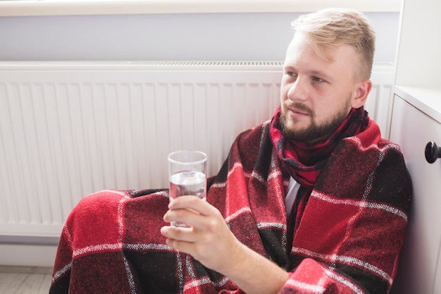 Bezpłatne zdjęcie mężczyzna pod kocem trzyma szkło woda