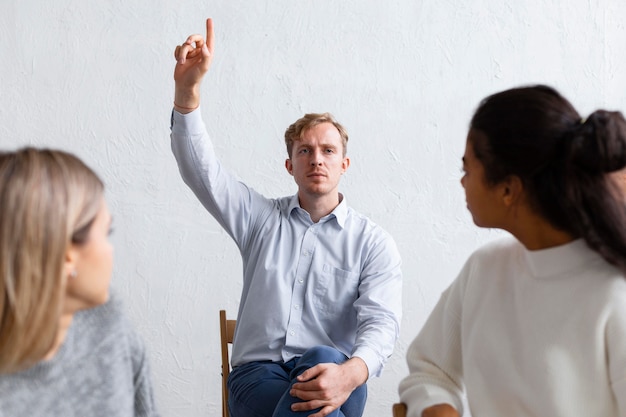 Mężczyzna podnosi rękę do pytania na sesji terapii grupowej