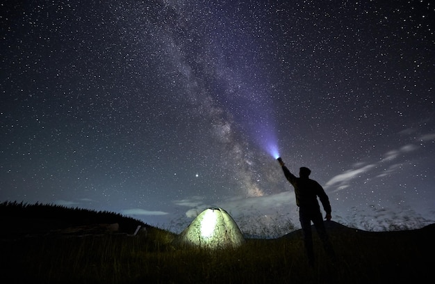 Mężczyzna podróżnik świecący latarką w nocne rozgwieżdżone niebo