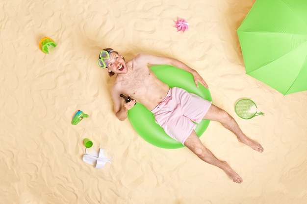 Mężczyzna pozuje na zielonym pływackim ringu z piwem nosi szorty maska do nurkowania spędza wolny czas na plaży odpoczywa latem radośnie spogląda w kamerę