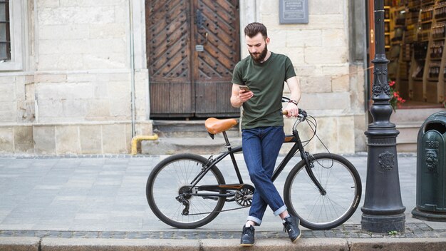 Mężczyzna pozycja z jego bicyklem używać smartphone