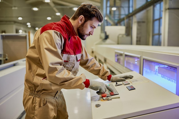 Mężczyzna pracownik obsługujący zautomatyzowaną maszynę linii produkcyjnej w fabryce obróbki drewna