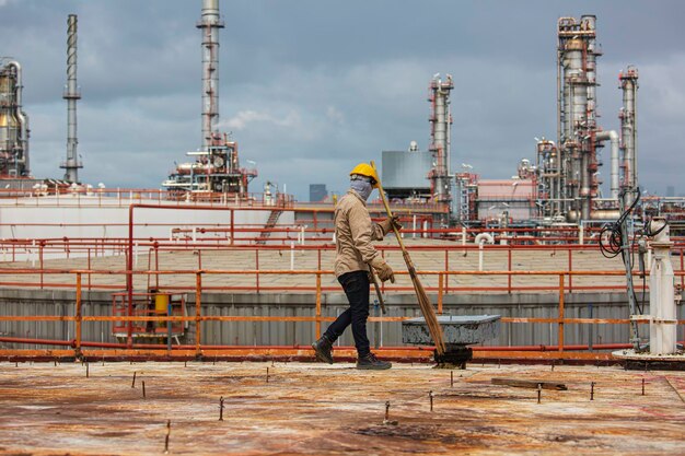 Mężczyzna pracownik ubrany w odzież ochronną czyszczenie dachu zbiornik do przechowywania oleju konstrukcja przemysłowa