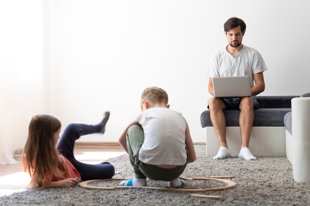 Mężczyzna próbuje pracować na laptopie w domu, podczas gdy jej dzieci biegają dookoła