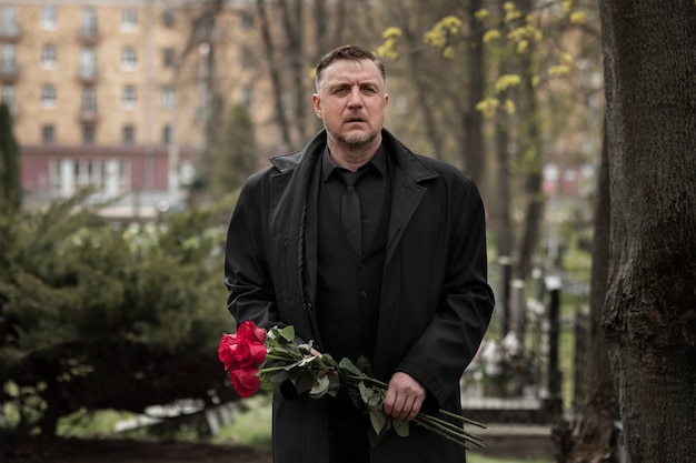 Bezpłatne zdjęcie mężczyzna przynoszący róże na nagrobek na cmentarzu