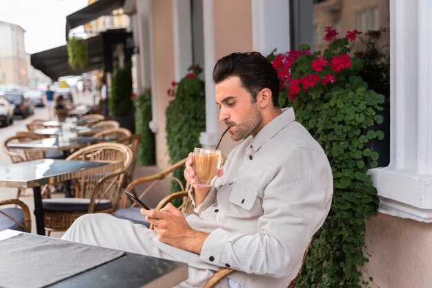 Mężczyzna robi przerwę na mrożoną kawę podczas korzystania ze smartfona