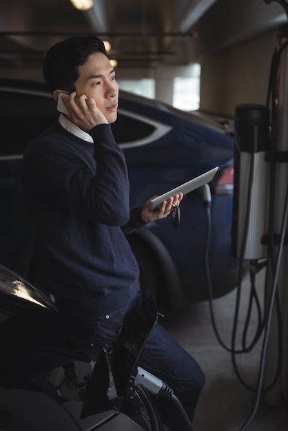Mężczyzna rozmawia przez telefon komórkowy podczas ładowania samochodu elektrycznego