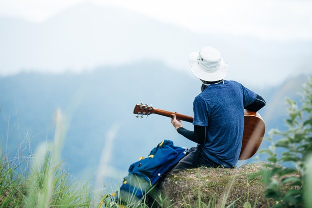 Mężczyzna siedzący szczęśliwie grający na gitarze sam w lesie.