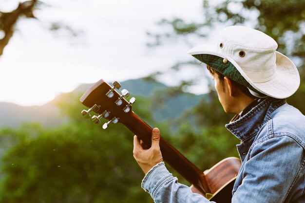 Mężczyzna siedzący szczęśliwie grający na gitarze sam w lesie.