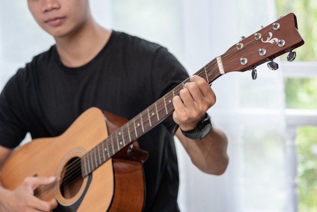 Mężczyzna Siedzi I Gra Na Gitarze Na Krześle.