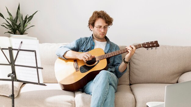 Mężczyzna siedzi na kanapie i uczy się gitary