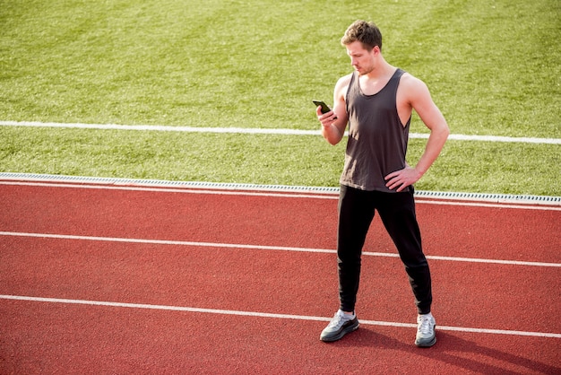 Mężczyzna sportowiec stojący na torze wyścigowym za pomocą telefonu komórkowego