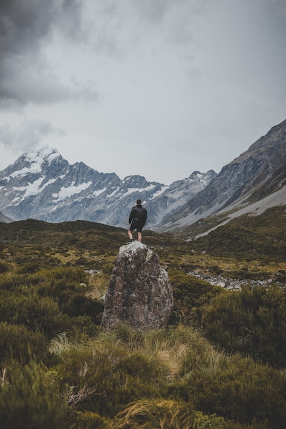 Bezpłatne zdjęcie mężczyzna stojący na kamieniu w hooker valley track z widokiem na mount cook w nowej zelandii