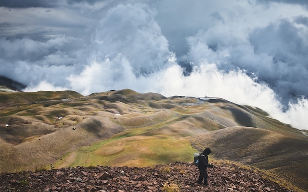 Mężczyzna stojący na wzgórzu pokrytym zielenią pod burzowym niebem w ciągu dnia